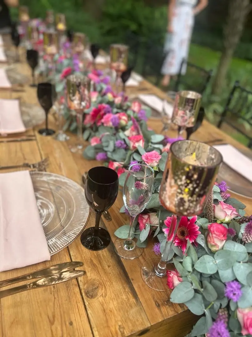Pink roses, magenta gerberas and purple blooms along a timber table with rose-gold goblets and blush napkins