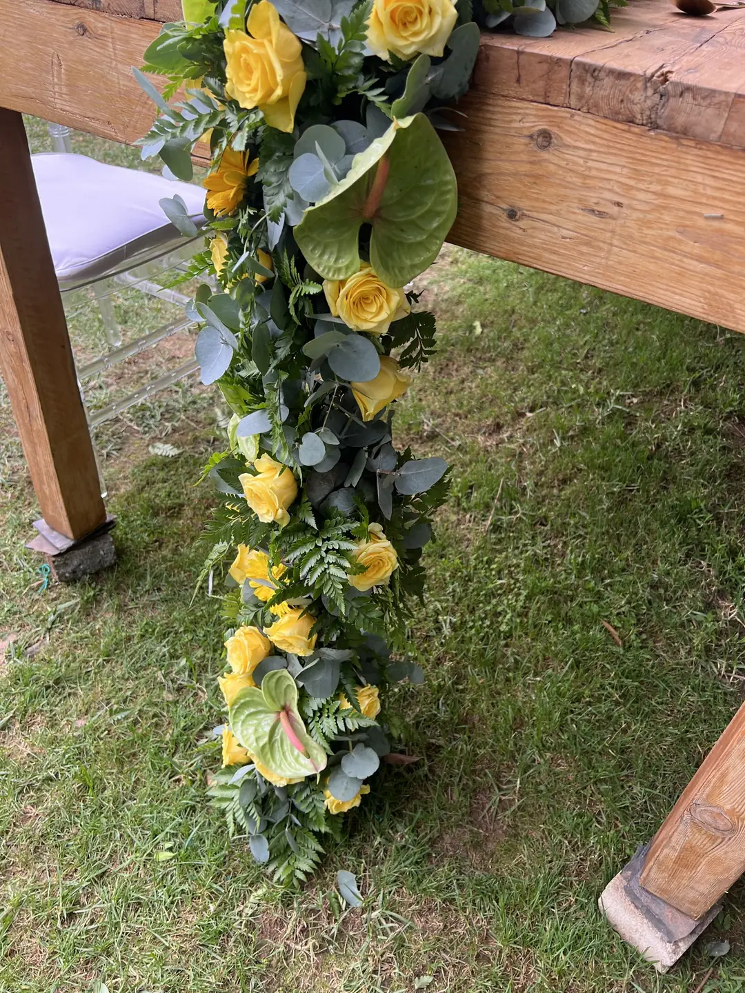 Garland of yellow roses, lime anthuriums, ferns and eucalyptus cascading from the edge of a timber table to the lawn