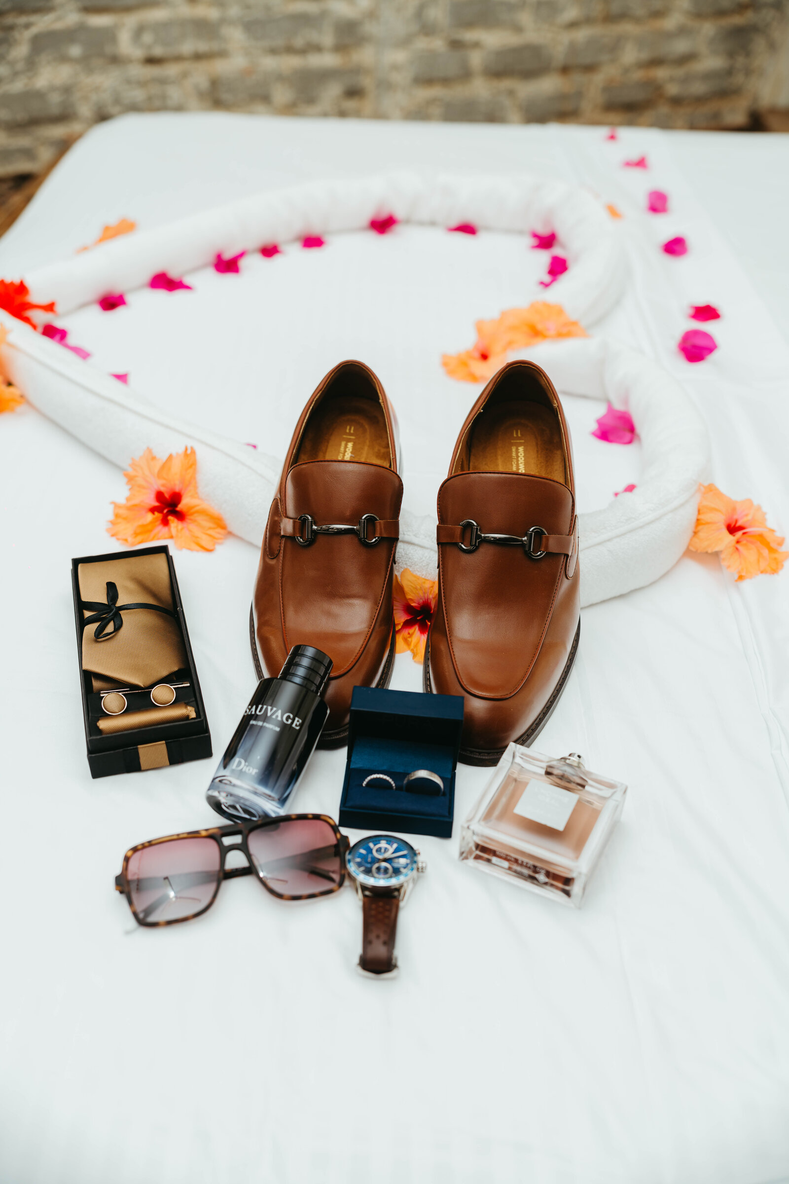 Groom's styling flat lay with leather loafers, cufflinks, cologne and sunglasses